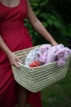 a woman in a red dress holding a wicker basket filled with baby blankets and shoes