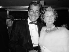 an old black and white photo of two people dressed in formal wear smiling for the camera