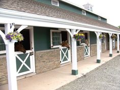 two horses sticking their heads out of the windows of a horse stable with flowers hanging from them