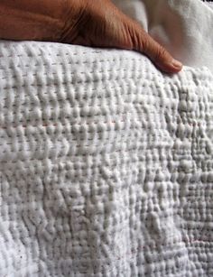 a person's hand resting on the edge of a bed with white linens