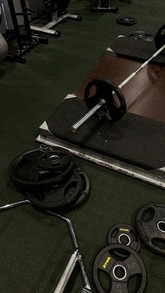 a gym floor with various weight plates and barbells on it, including a pair of exercise wheels