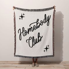 a woman holding up a white and black blanket with the words somebody club on it