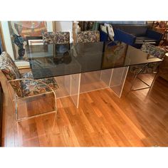 a glass dining table with two chairs and a couch in front of it on a hard wood floor