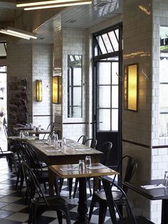 an empty restaurant with black and white checkered flooring, large windows, and wooden tables