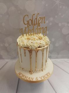 a wedding cake with white frosting and gold lettering on top, sitting on a table