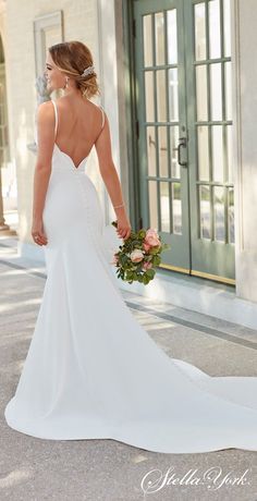 a woman in a white wedding dress is holding a bouquet and looking down at the ground