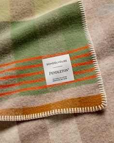 a plaid blanket with an orange, green and brown stripe on the bottom is shown