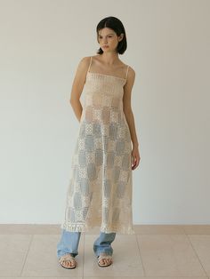 a woman standing in front of a white wall wearing a dress with crochet