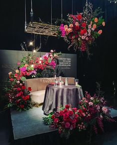 an arrangement of flowers and candles on display at a flower show, with hanging lights above the tables