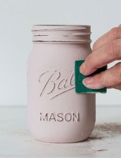 a person is cleaning a mason jar with a green sponge to clean the paint off