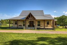 a small brick house with a metal roof in the middle of a grassy field next to a dirt road