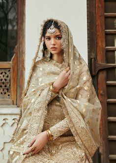 a woman in a white and gold bridal outfit posing for the camera with her hands on her hips