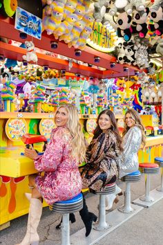 three women sitting on stools in front of a carnival ride