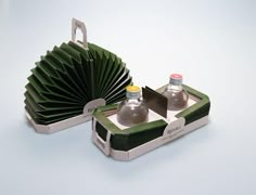 two empty bottles are sitting in a green and white box with folded fan on top