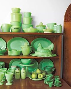 a wooden shelf filled with green dishes and cups