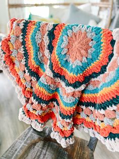 a crocheted blanket sitting on top of a wooden table next to a chair