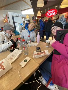 three people sitting at a table with drinks in front of them and one person taking a selfie