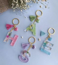 four key chains with letters and tassels hanging from them on a blue surface