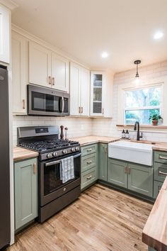 a kitchen with green cabinets and white walls, wood flooring and stainless steel appliances