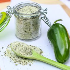 two green peppers sitting on top of a cutting board next to a jar of seasoning