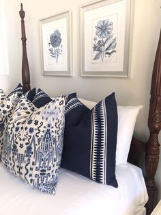 four pillows on a bed with white sheets and wooden posts in the background, framed pictures above them