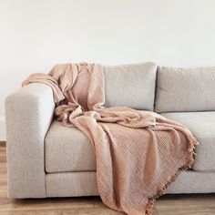 a couch with a blanket on it in front of a white wall and wooden floor