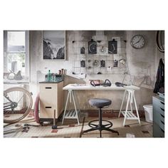 a room with a desk, bike and various objects on the wall behind it in front of a window