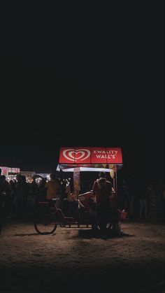 a group of people standing around a food stand at night