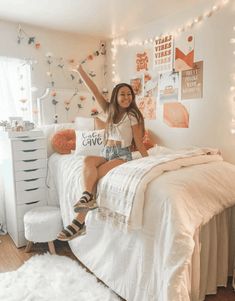 a woman sitting on top of a bed in a room with lights strung above her