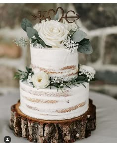 a wedding cake with white flowers and greenery is on top of a tree stump