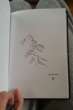 a hand holding an open book with a drawing of a mountain on the inside of it