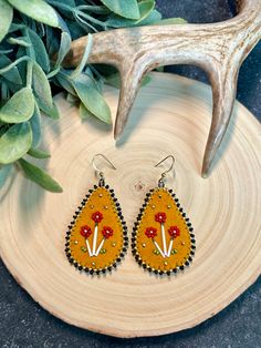 a pair of yellow and black earrings with flowers on them next to a deer's antler