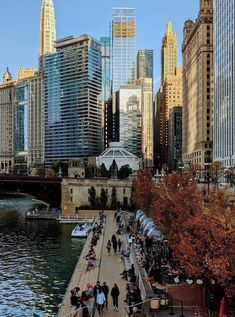 people are walking along the river in front of tall buildings and skyscrapers on either side