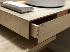 a close up of a drawer on a table with a bowl and remote control in the background