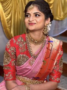 a woman in a red and yellow sari with gold jewelry on her head, smiling at the camera