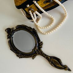 an antique mirror sitting next to a pearl necklace on a white counter top with a purse in the background