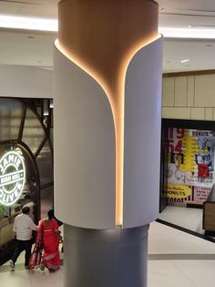 people are walking around in the lobby of a shopping mall, with an unusual light sculpture