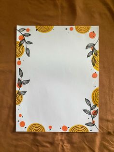 a piece of paper with oranges and leaves on it sitting on a sheet of brown fabric