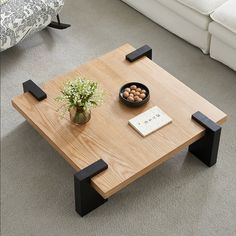 a coffee table with two black legs and a bowl of nuts on top, sitting in front of a white couch