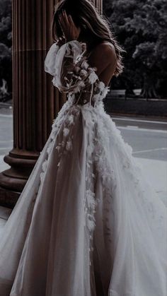 a woman in a wedding dress standing next to a pillar with her hand on her face