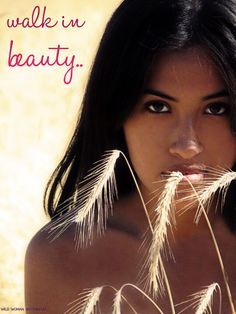 a beautiful young woman standing in front of some dry grass and looking at the camera