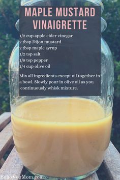 a glass jar filled with liquid sitting on top of a wooden table next to a sign that says maple mustard vinaigrete