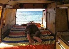 a man laying on top of a bed in the back of a van next to the ocean