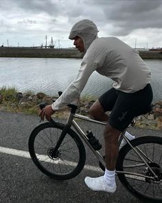 a man riding a bike down a street next to a body of water on a cloudy day