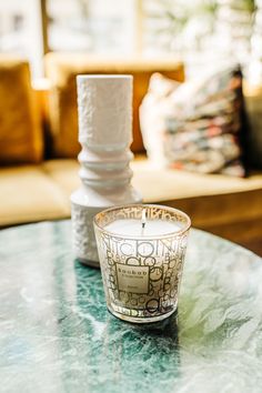 a glass candle holder sitting on top of a table in front of a couch with pillows