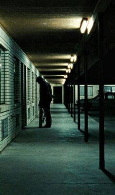 a person with a suitcase walking down an empty hallway in the dark, at night