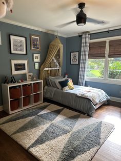 a bedroom decorated in blue and white with a bed, rugs, windows, and pictures on the wall