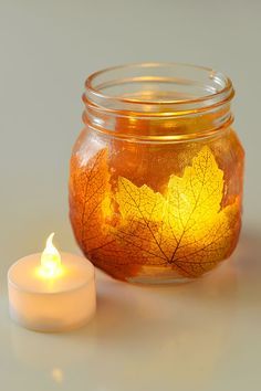 a lit candle sitting next to a jar filled with leaves