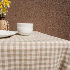 a table topped with a white plate and bowl next to a vase filled with yellow flowers