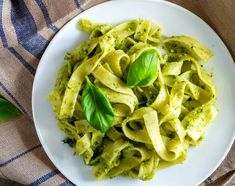 a white plate topped with pasta covered in pesto sauce and green leafy garnish